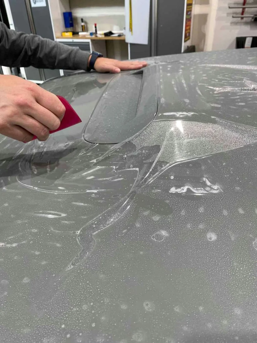 Installer using a squeegee to apply clear paint protection film to a gray vehicle panel