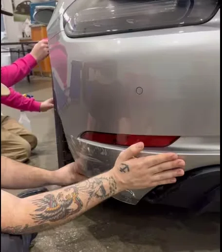 APC installers fitting clear film along the lower edge of a rear bumper